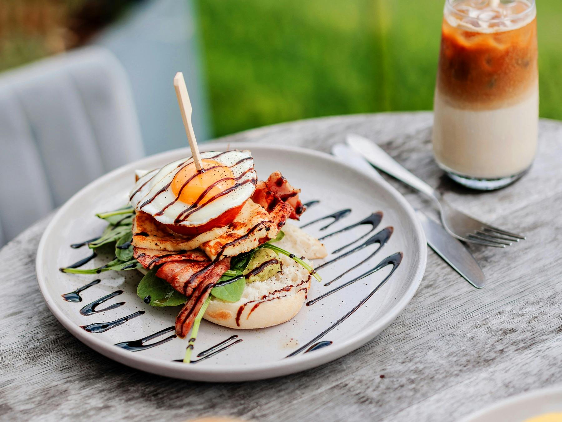 Brekkie stack with halloumi, avo, roasted tomato, fried egg, bacon, spinach, and balsamic glaze