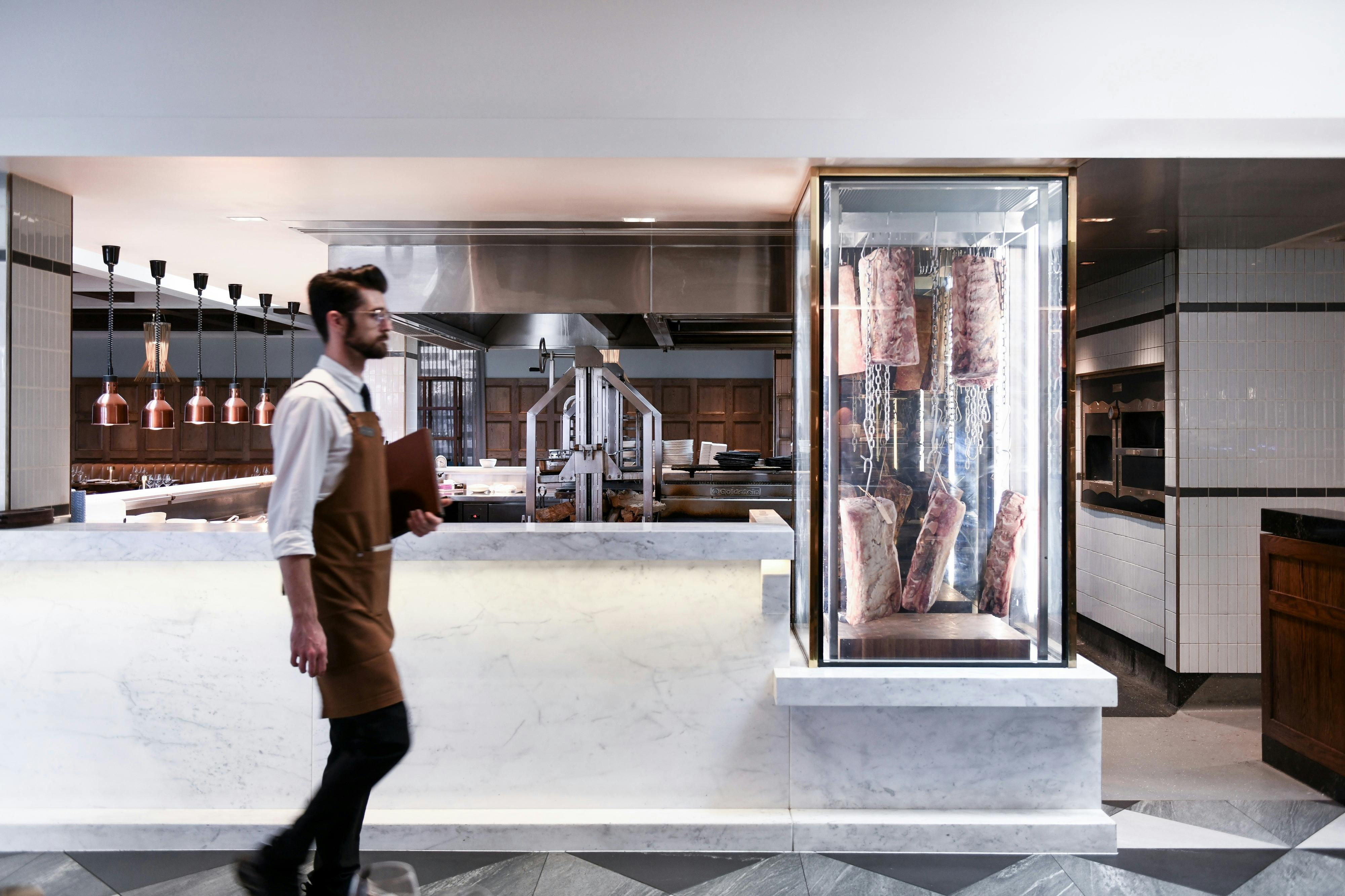 Modern restaurant with open kitchen, marble finishes, and premium meat display.