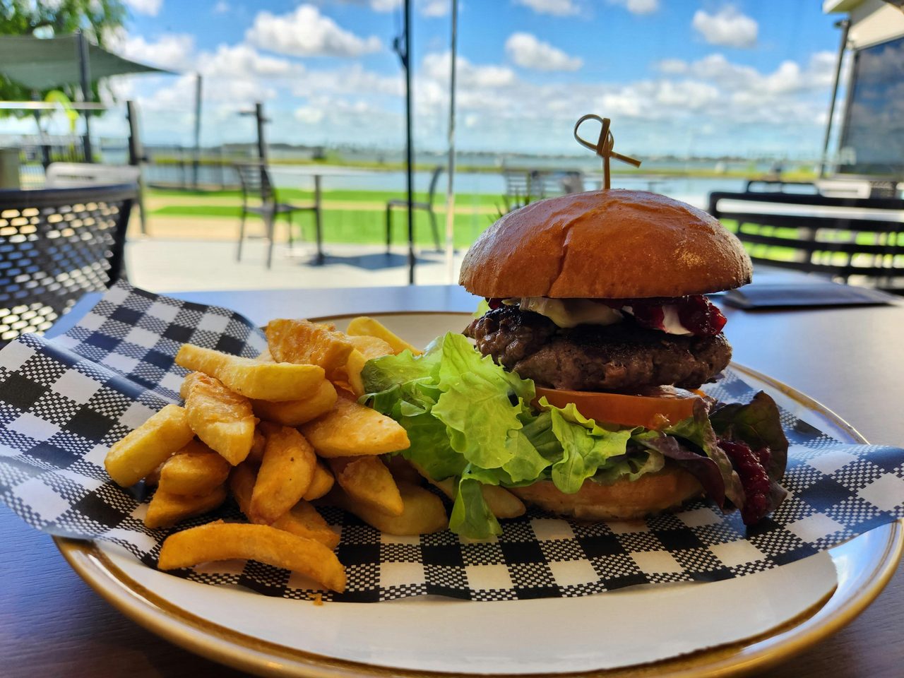 Wagyu Beef Burger served with a side of chips and a beautiful waterside view.