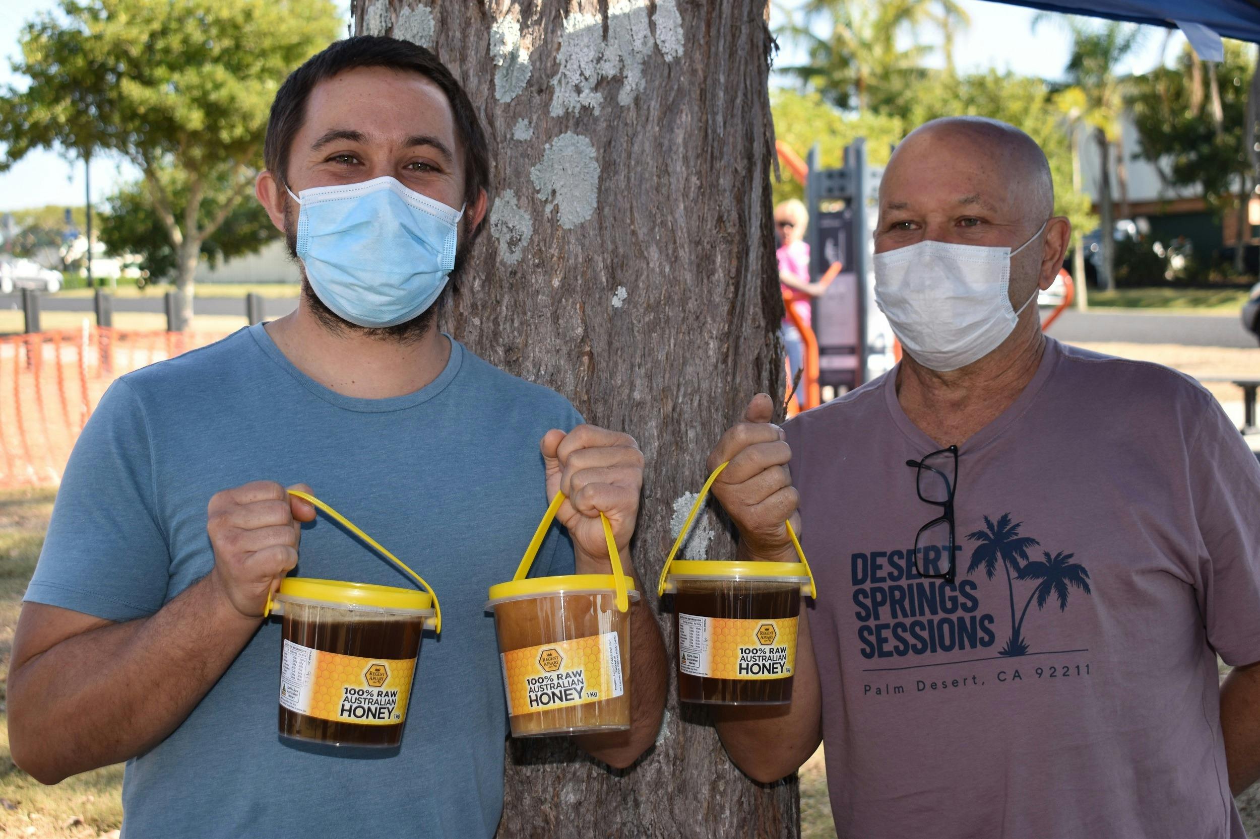 Two men holding buckets of honey.