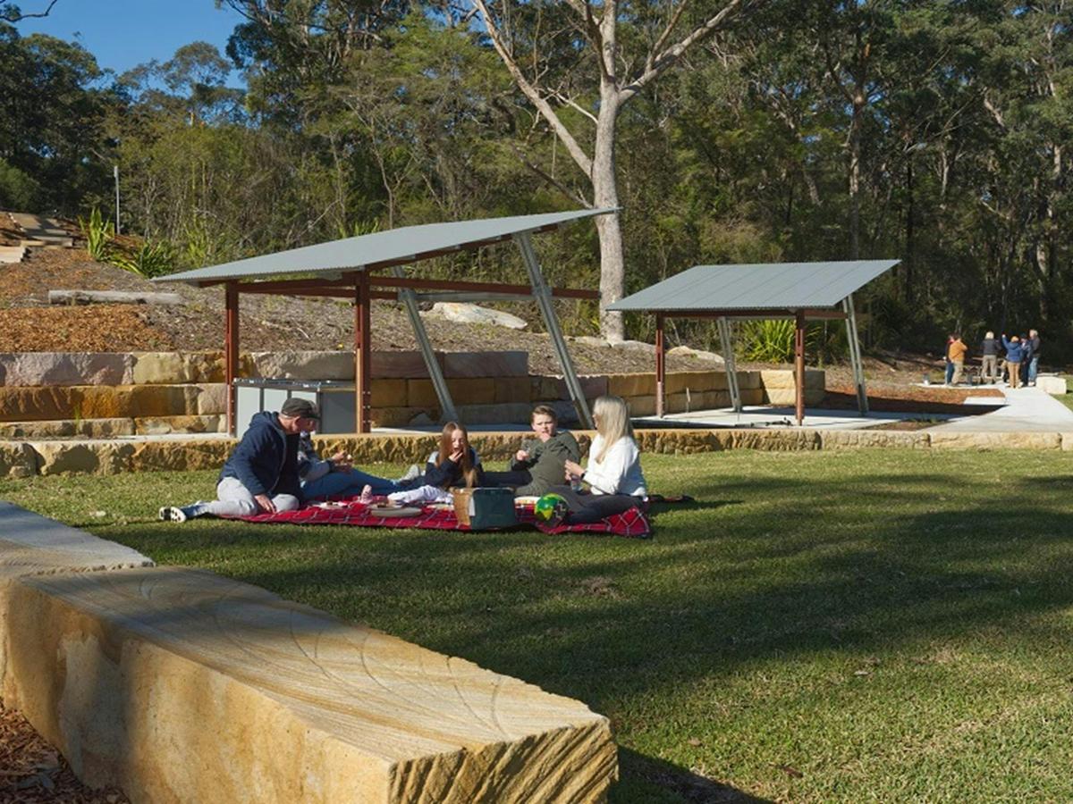 A family shares a picnic lunch on the grass at Somersby Falls picnic area, Brisbane Water National