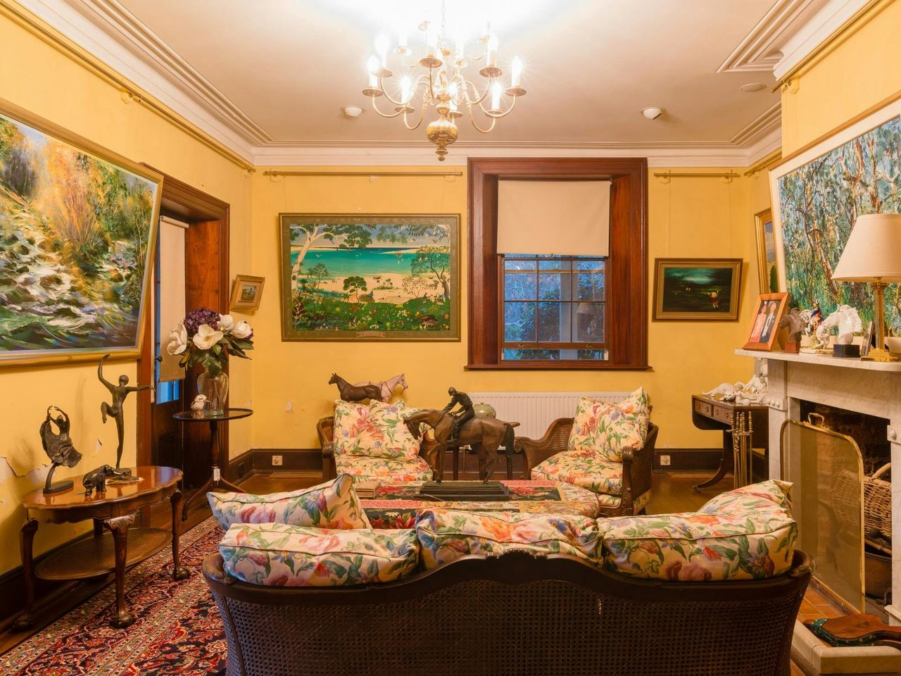 Inside a historic house. Room has yellow walls, ornate furniture and a lit chandeleir.
