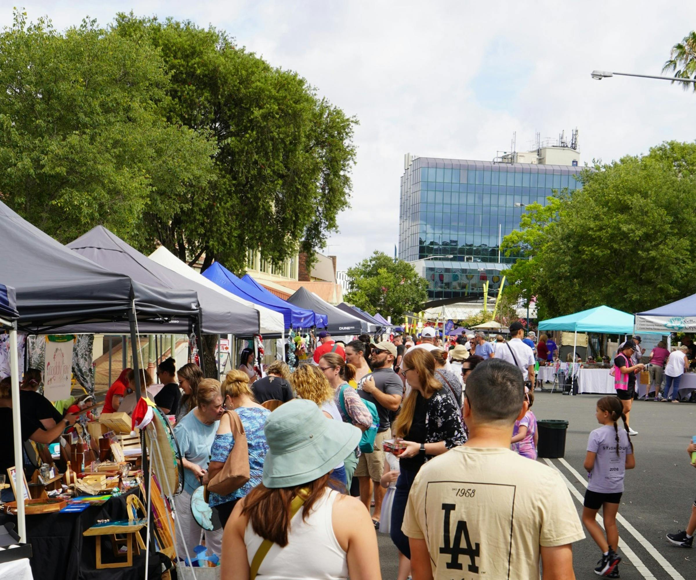 A large group of people are walking through the market looking at the stalls