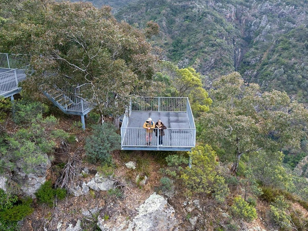 Two visitors look down into the bush and cliff face at Adams lookout and picnic area, Bungonia