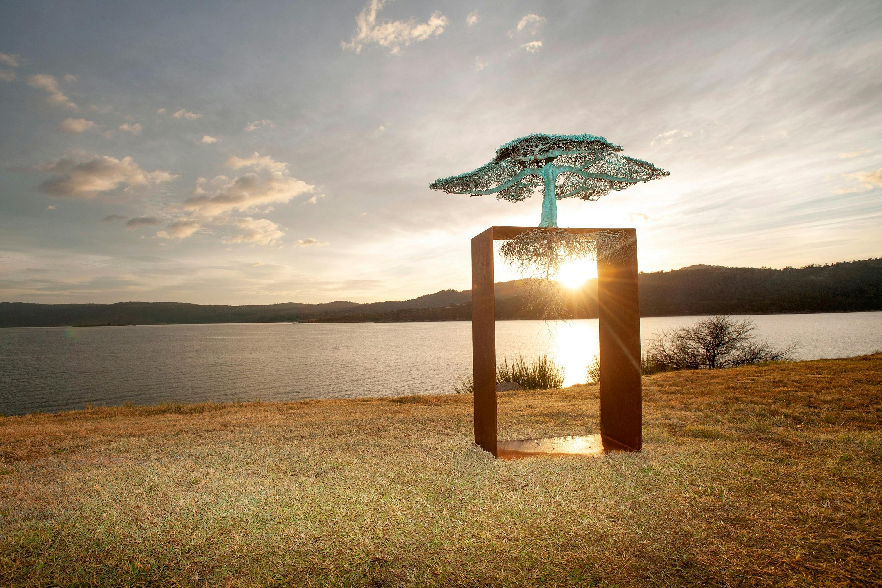 A metal tree sculpture in a square frame, with intricate branches and suspended roots.