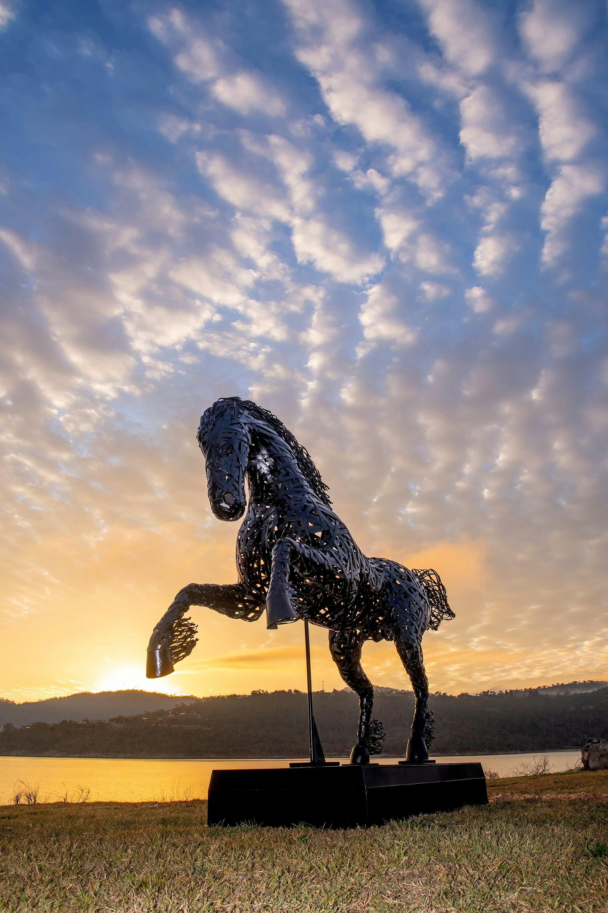 A stunning metal horse  rearing on its hindlegs, against a glowing sunset sky backdrop.
