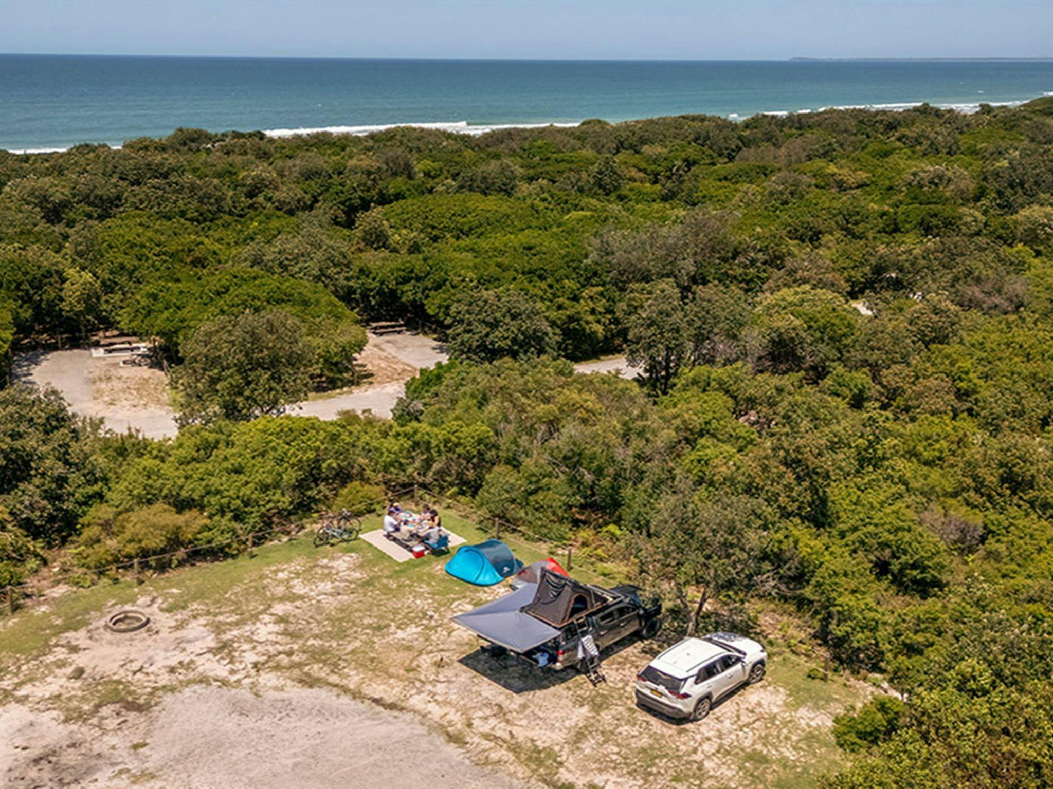 A group of campers camping beside their vehicle at Mibanbah-Black Rocks campground, the ocean in the