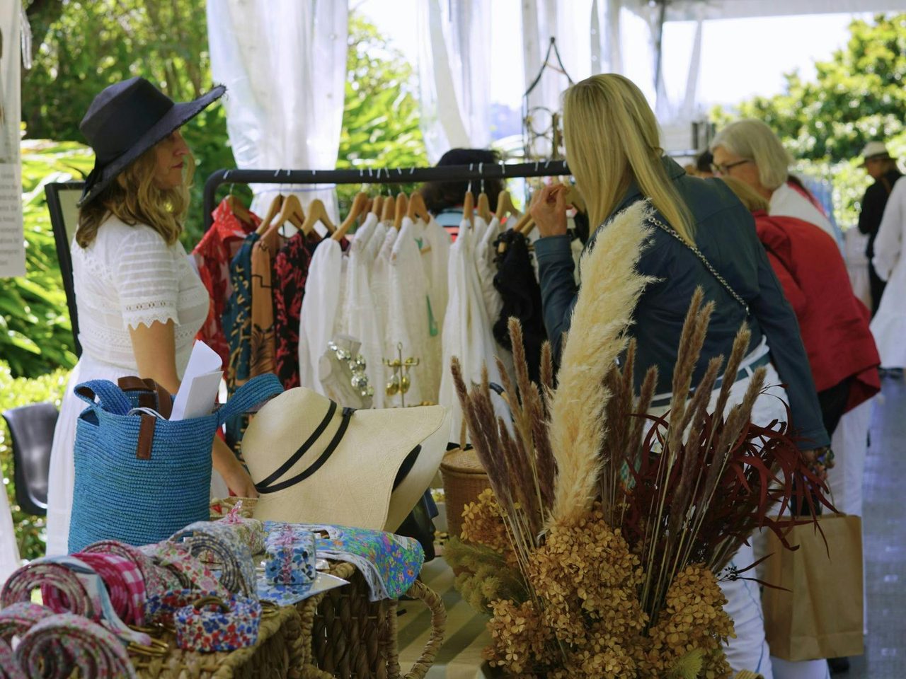 Two women shop looking at clothes on a rack at an outside  market
