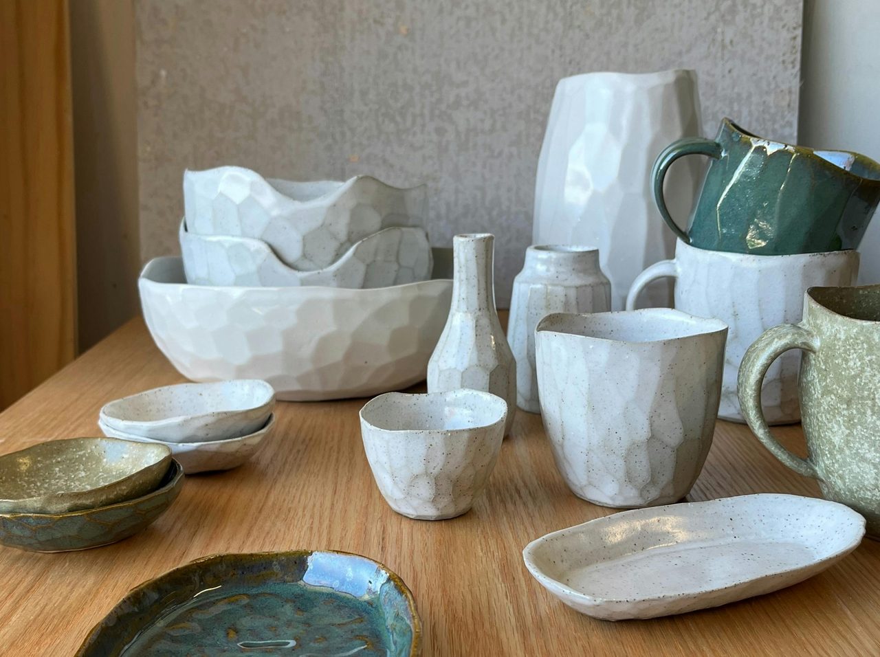 Woman with green shirt and glasses smiles while looking at cup in her hand shelves of pots behind