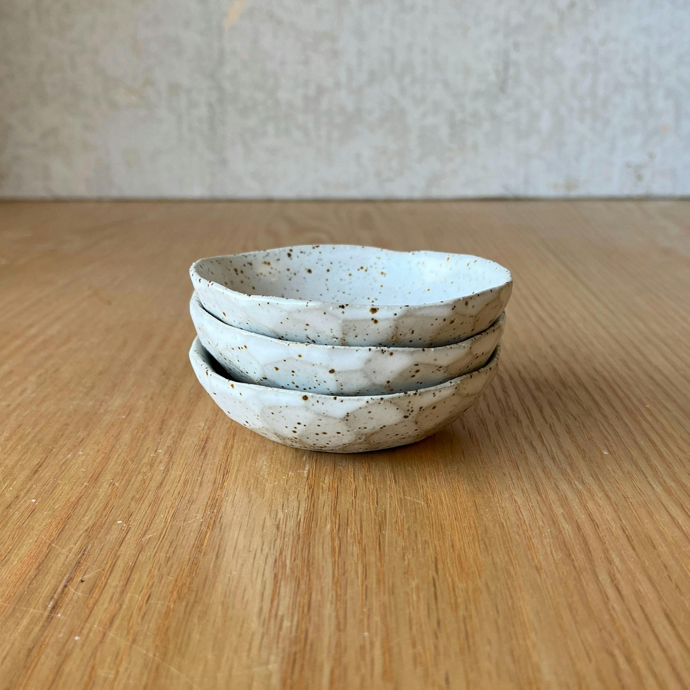 Stack of 3 speckled oil dishes on a wooden table with a grey background