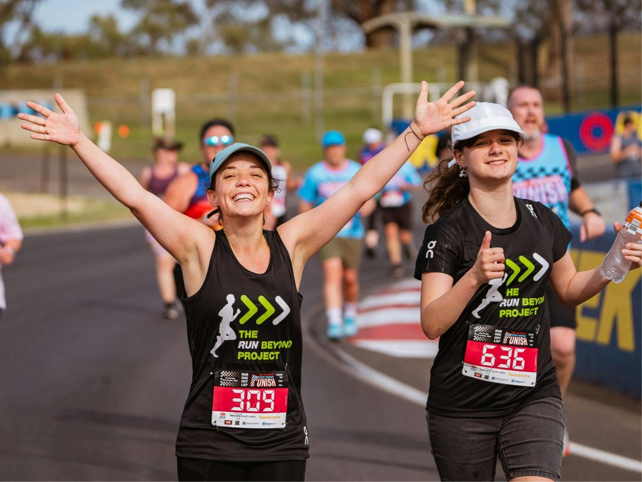 Two runners enjoying the Mount Panorama Punish, one with her hands in the air excitedly.