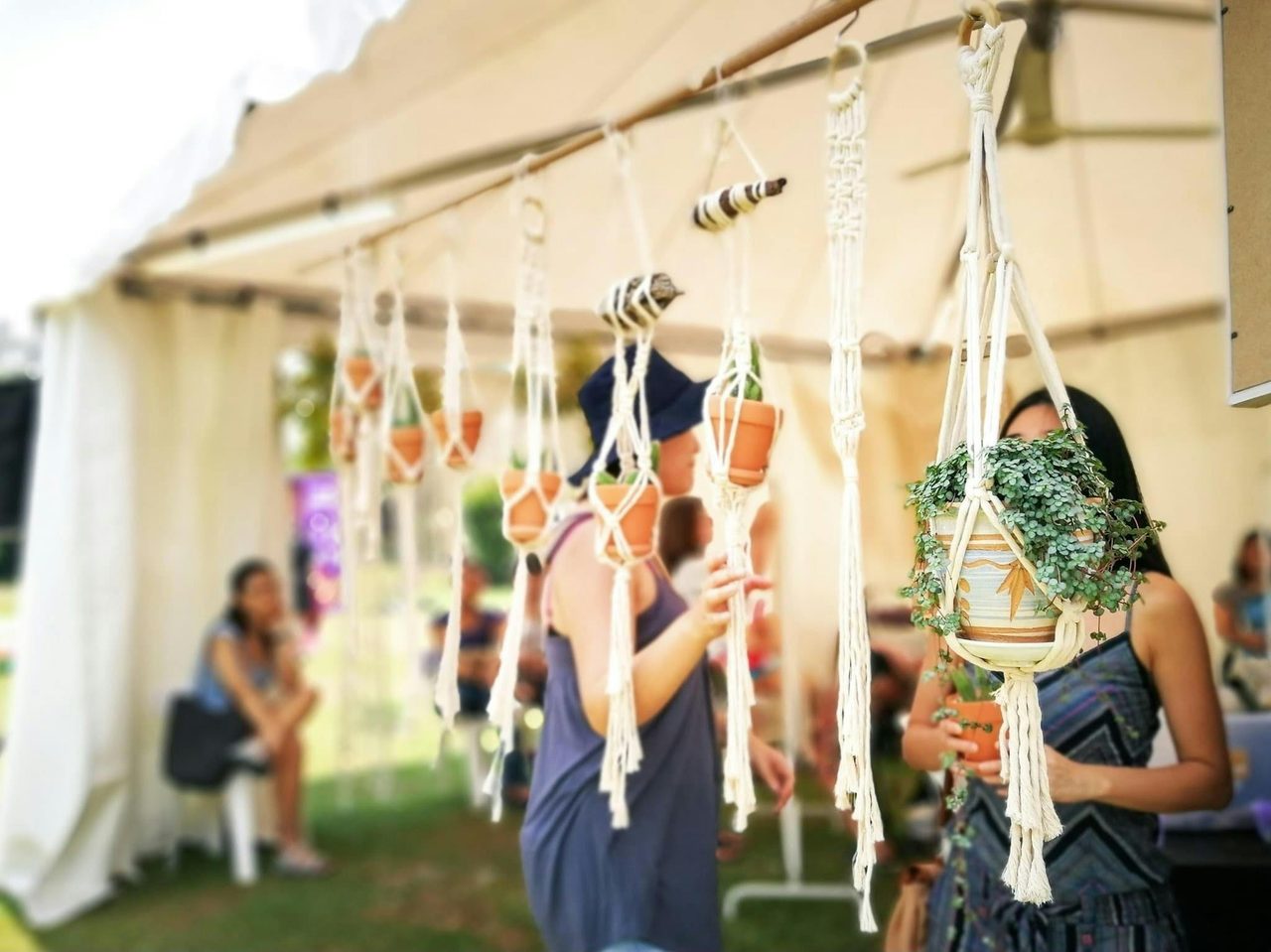 People browsing the offerings of a market stall, flower pots are hanging from the roof of the gazebo