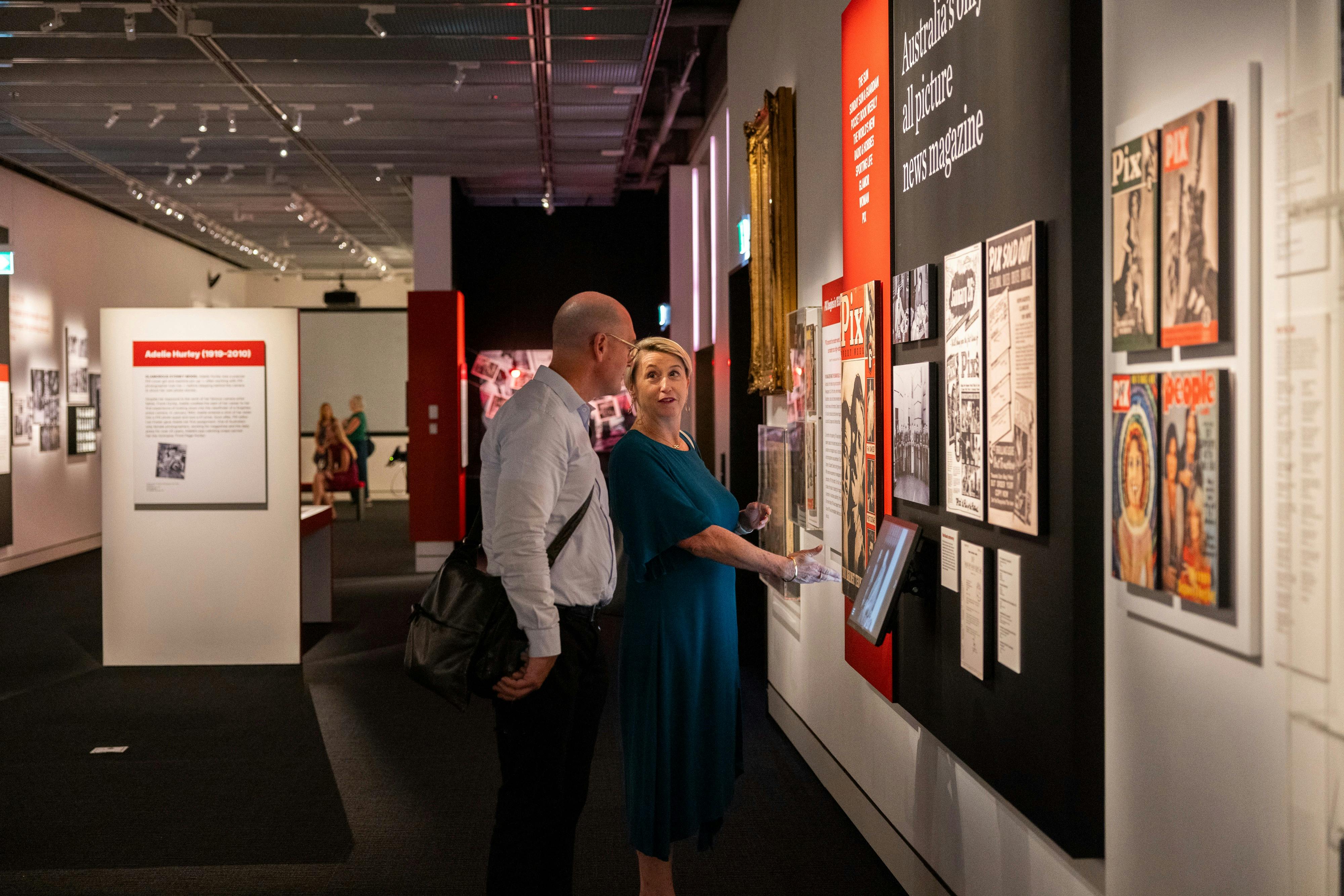 Two people in a exhibition with magazine covers and photography on display