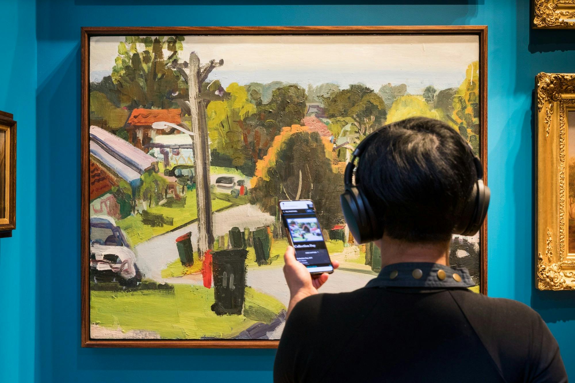 Person listening to an audio guide on their phone while standing in front of a painting