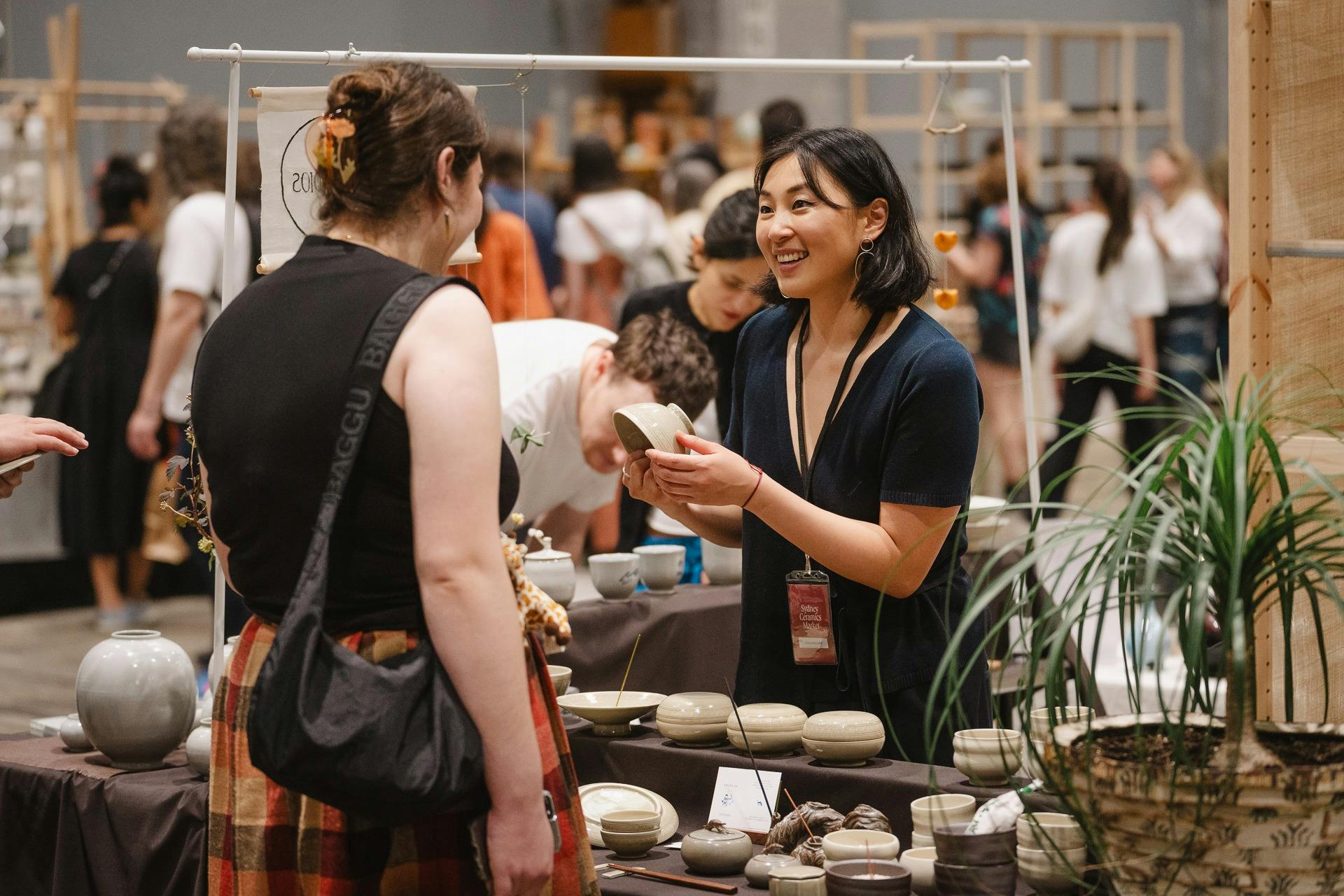 Artist and customer smile and discuss ceramic pieces at Sydney Ceramics Market