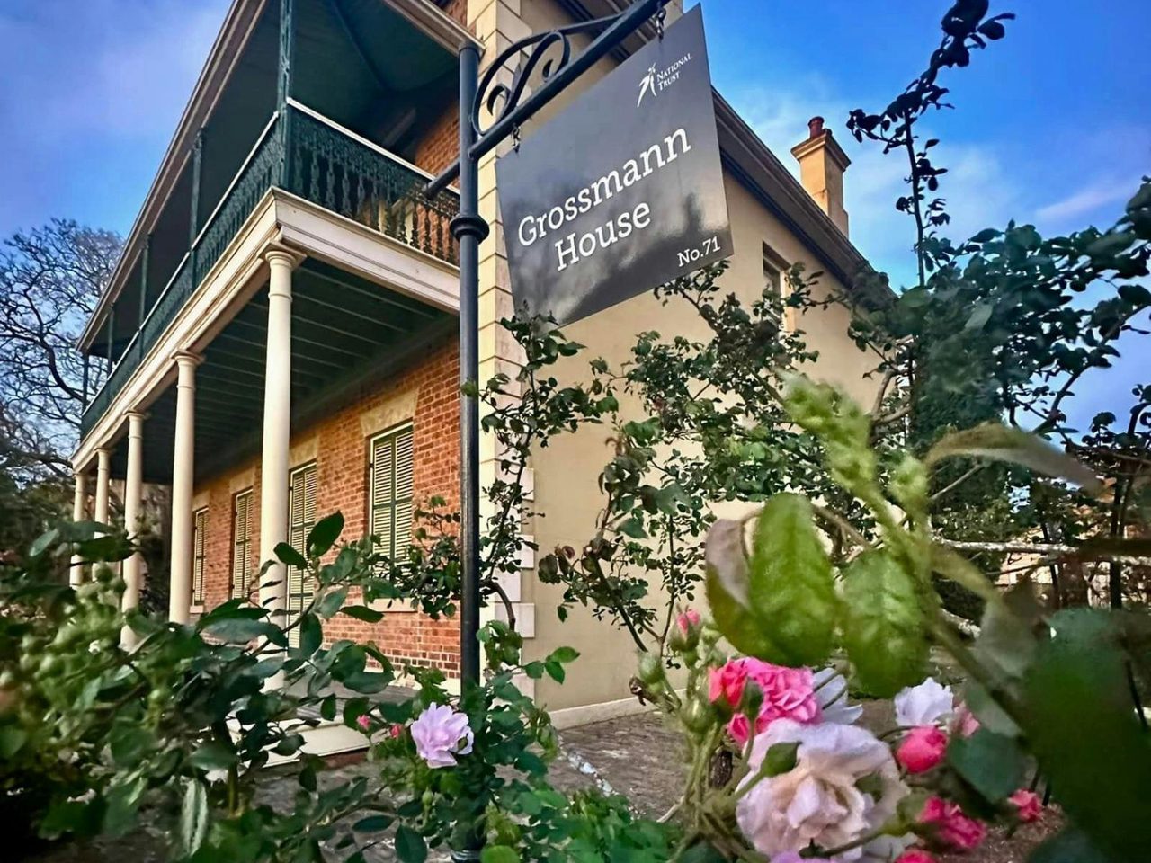 Twilight sets in over a double storey Victorian-era building. Roses fill the foreground