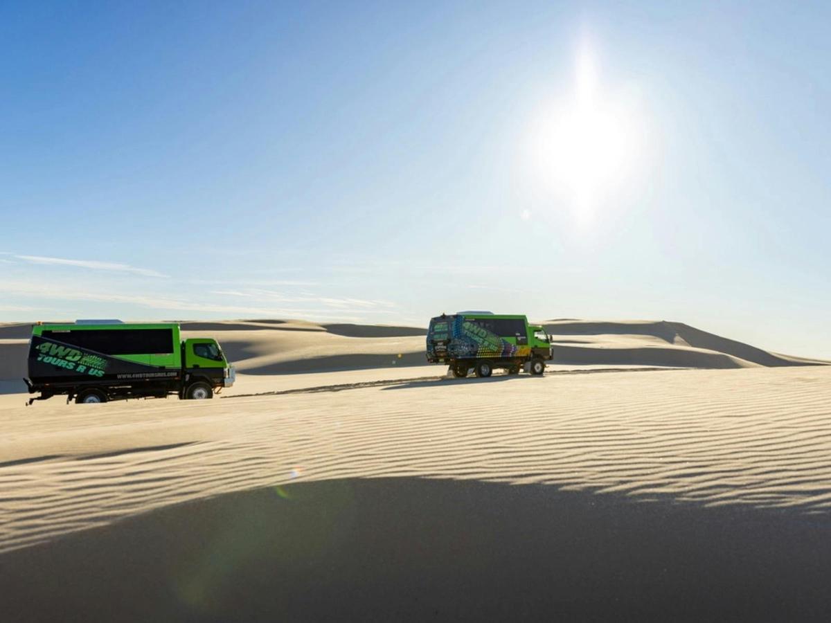 Two busses driving on sand dunes into the sun
