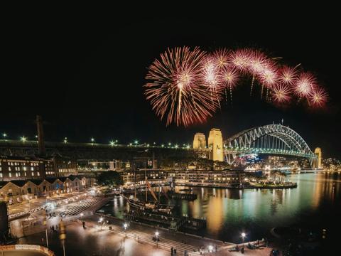 Fireworks bursting over Sydney Harbour Bridge at night, The Rocks precinct below