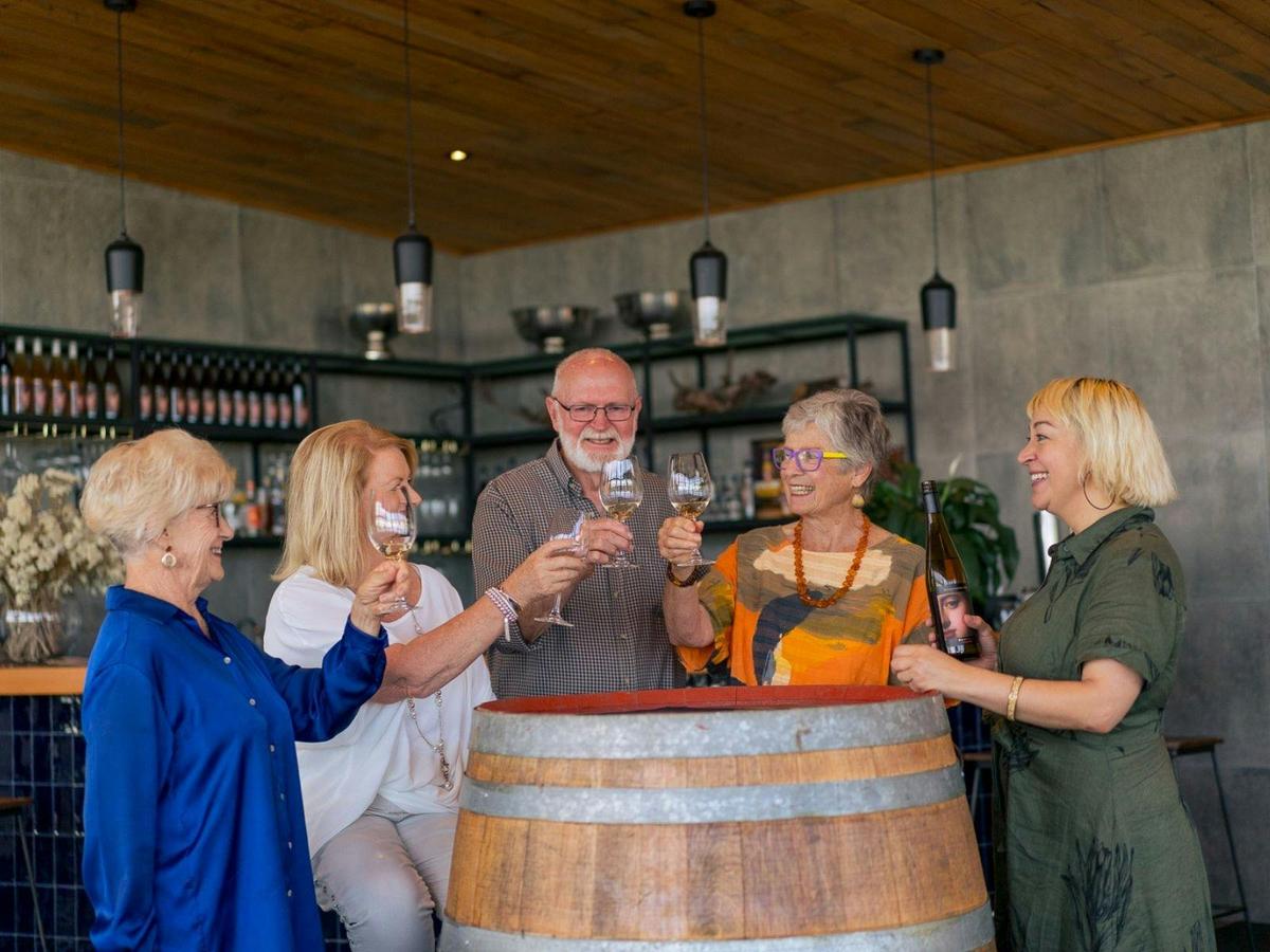 5 people standing at wine barrel tasting wine