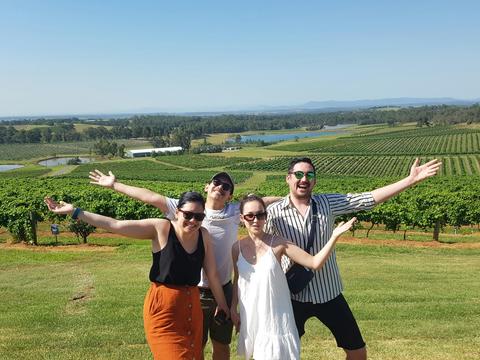 Four friends standing in front of a picturesque view of the vineyards in the Hunter Valley