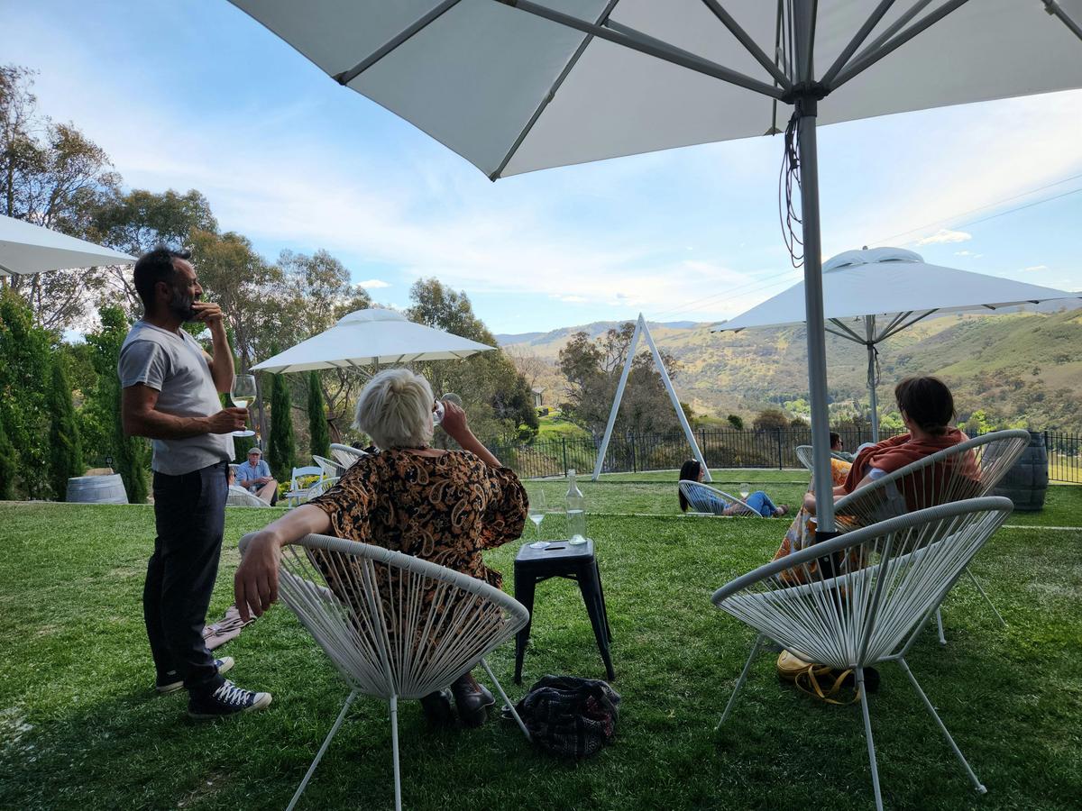 A man stands under an umbrella at a winery, seeking shelter from the rain.