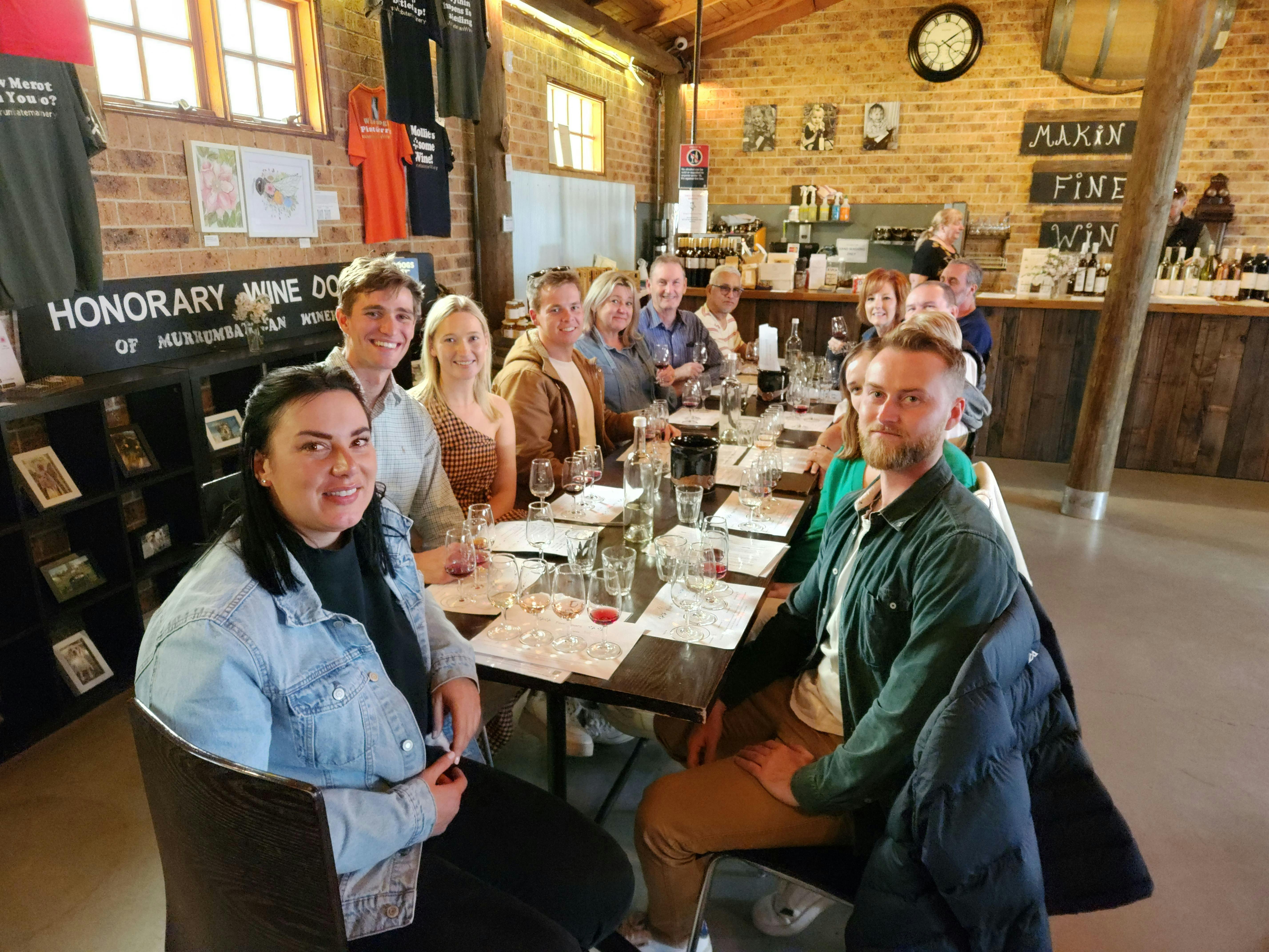 A group of people enjoying wine tasting at a table in a winery's tasting room.