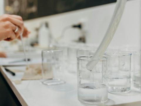 Tube dripping slowly into beaker with other beakers on bench in the background