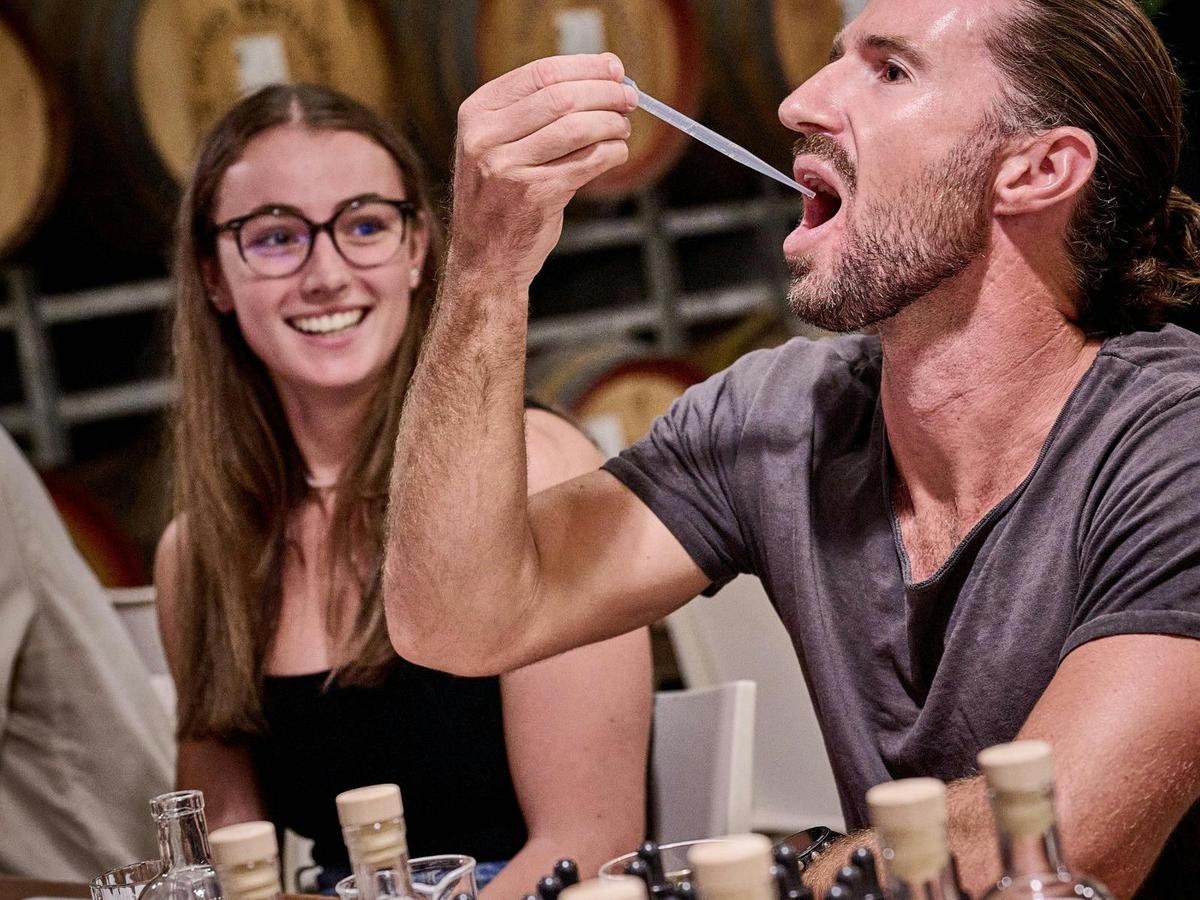 A woman smiles warmly as she watches a man tasting his spirit.