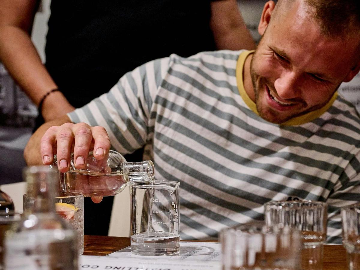 A man smiles as he pours his spirit into a beaker, carefully watching the liquid flow.