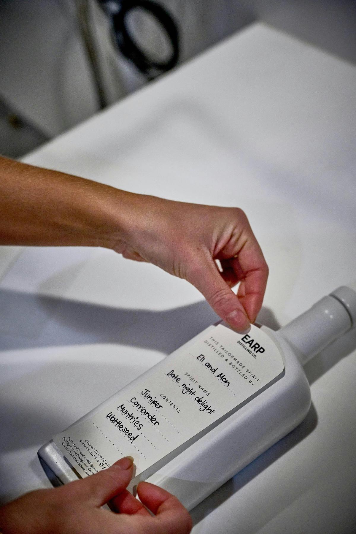 Hands carefully place handwritten label onto white bottle