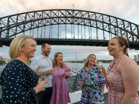 Guests unwinding on the outer decks of the Magistic sightseeing cruise, with Sydney Harbour Bridge i
