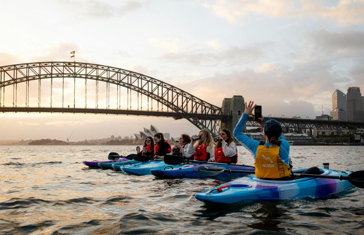Customers enjoy coffee from their kayaks on sydney harbour in front of the harbour bridge.