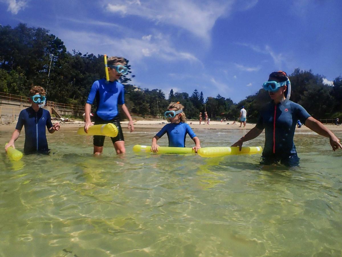 Four kids wade into the clear water with snorkel gear, ready for a fun underwater adventure