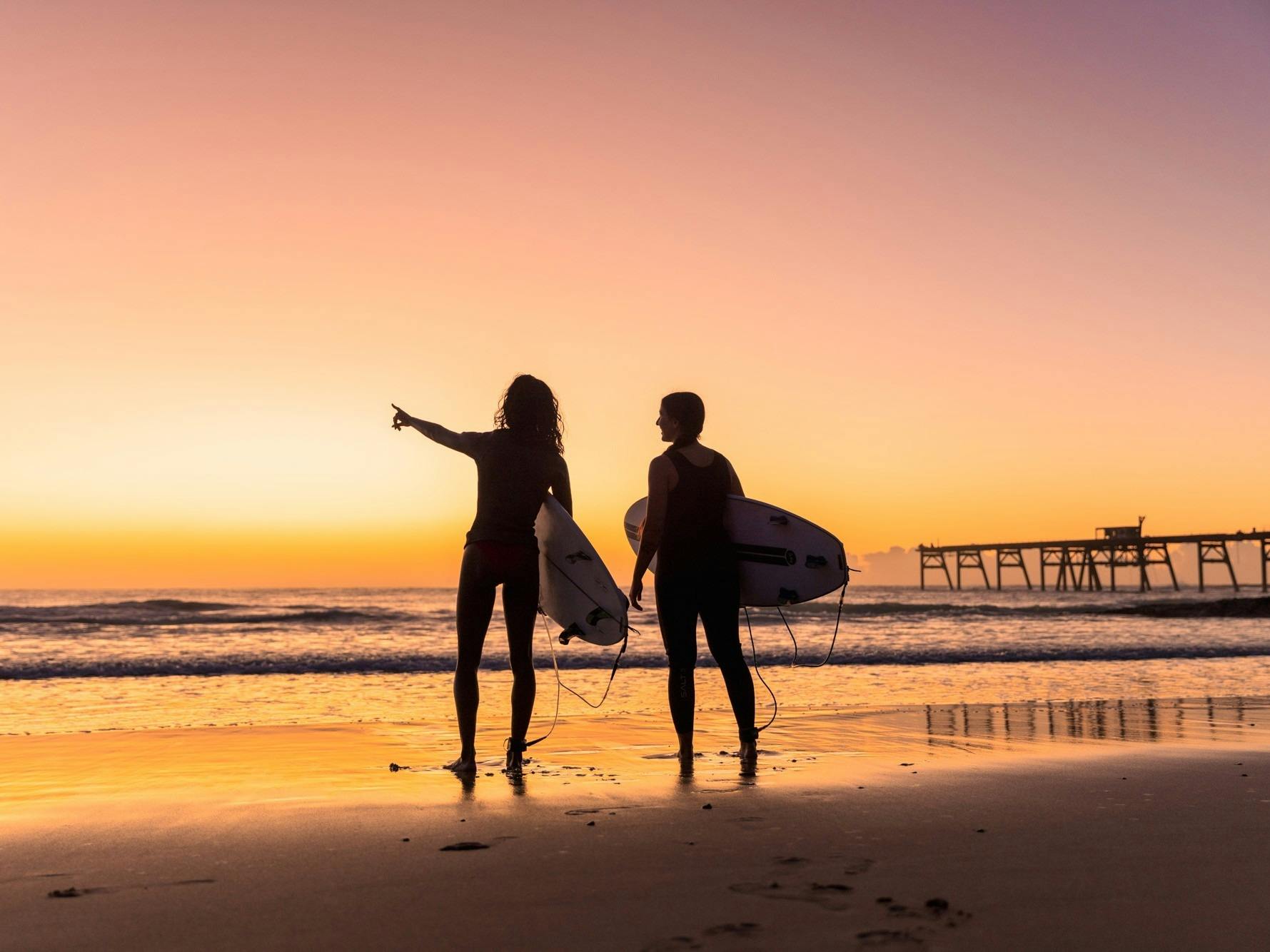 Surfers at sunrise with jetty in background