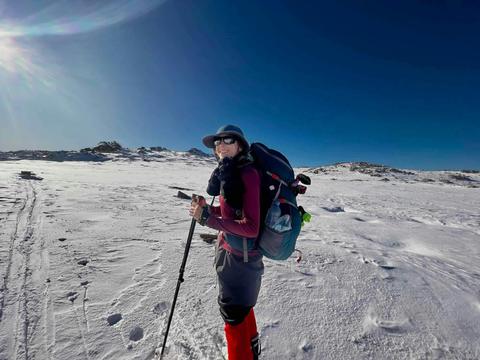 A hiker on a clear day walking through the snow with mountains in the distance.