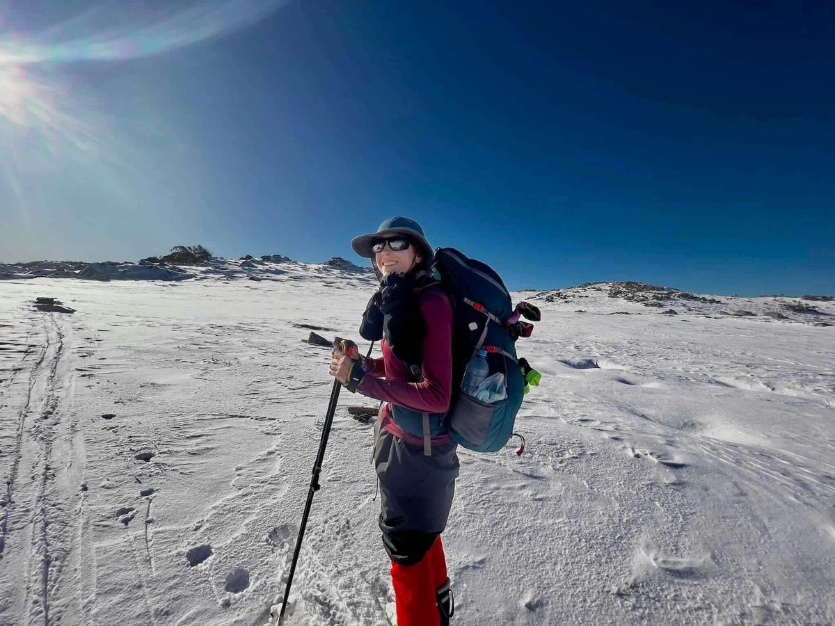 A hiker on a clear day walking through the snow with mountains in the distance.