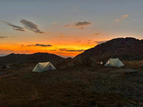 two tents in the mountains with the sun setting behind.