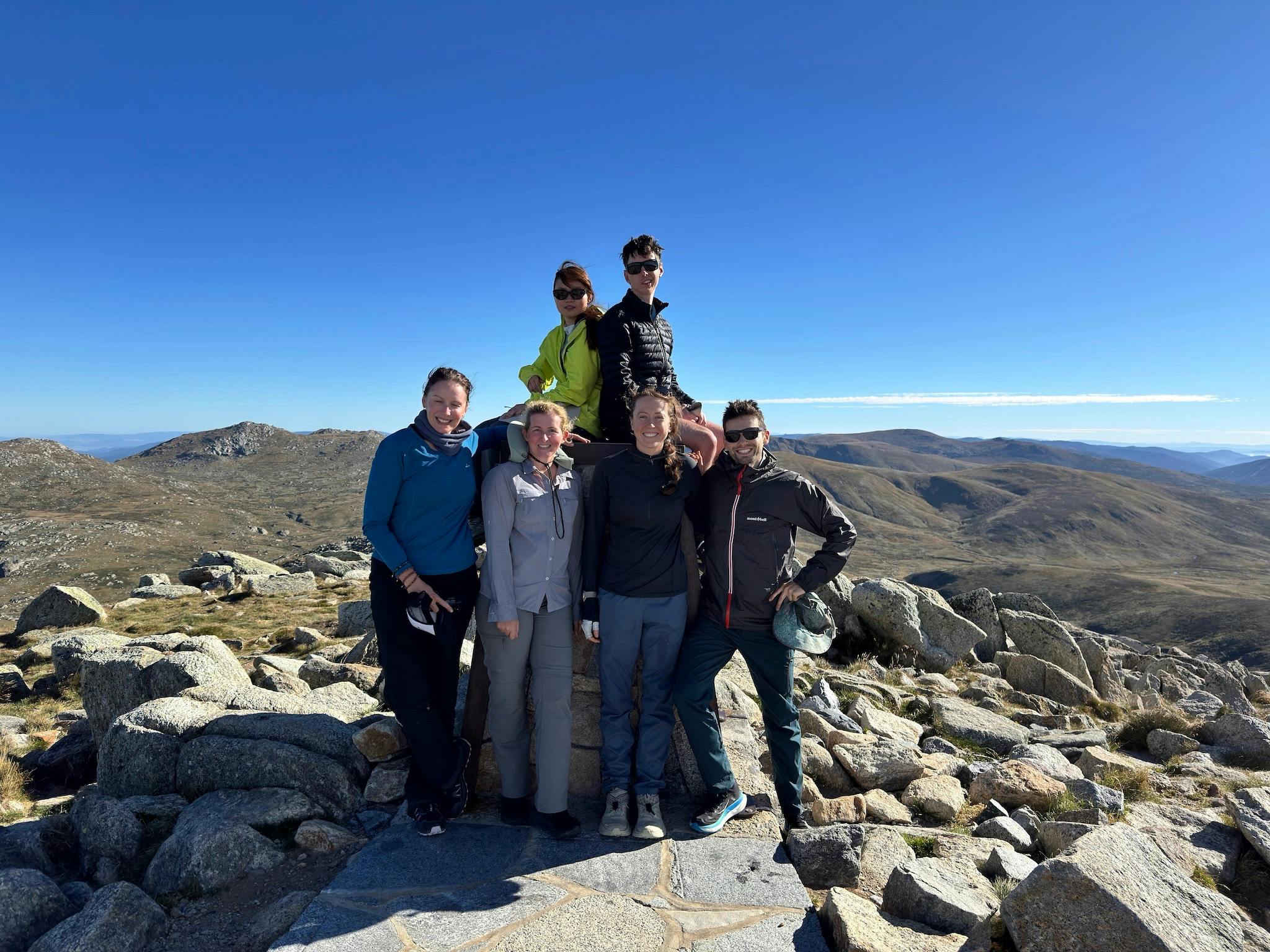 Six hikers at a mountain summit with blue skies