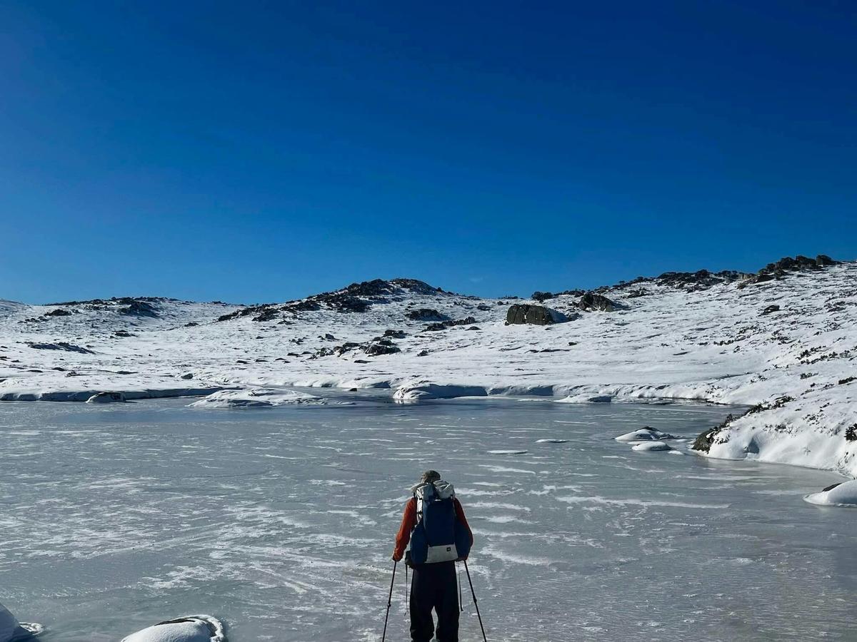 A hikers crossing a frozen lake in snowshoes with a clear blue sky in the background.
