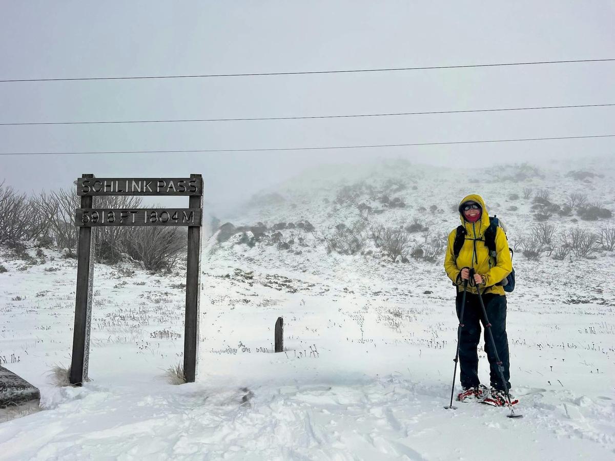 A hiker on snowshoes in a yellow jacket on snow covered mountains