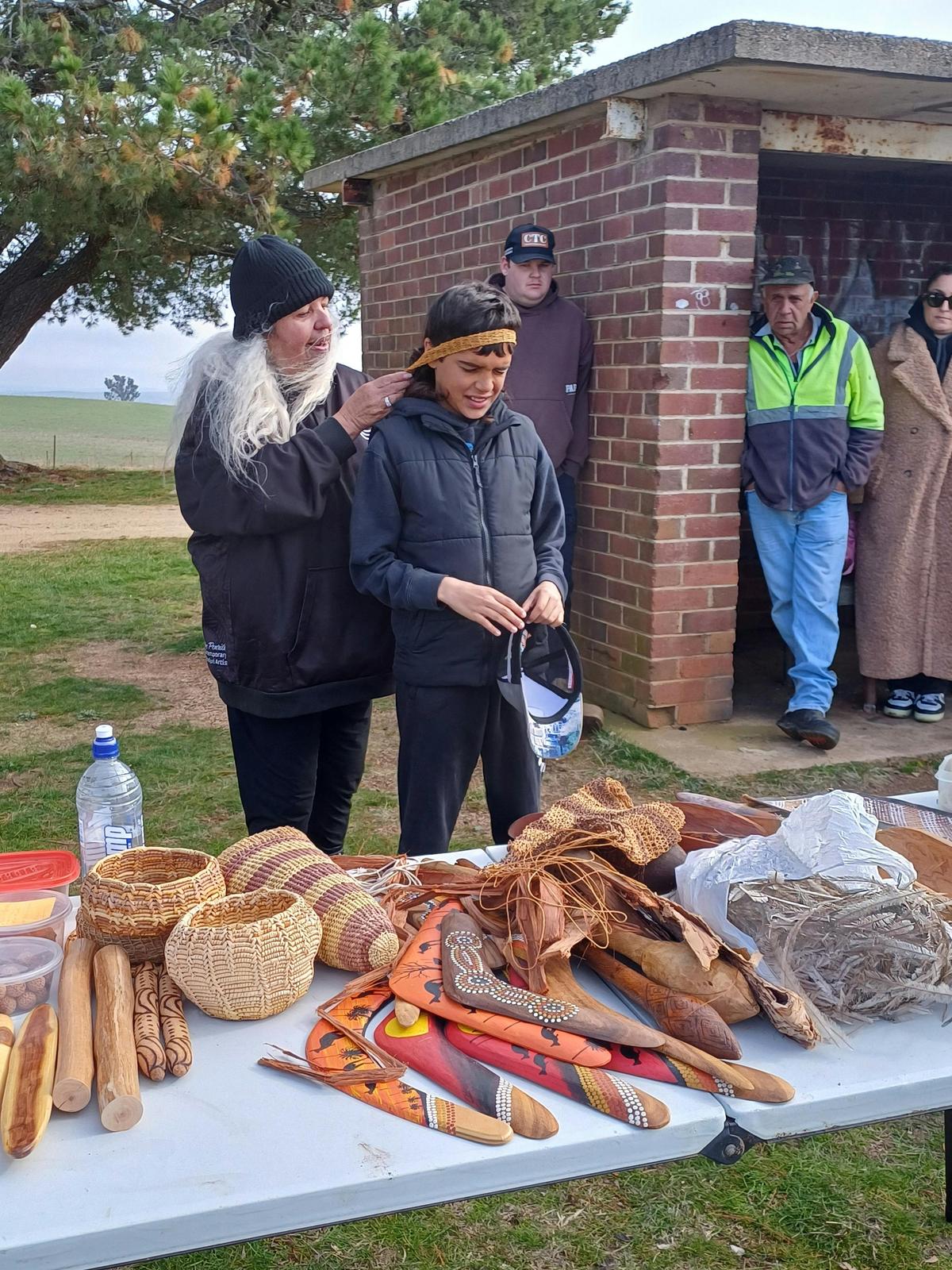 Aunty Enid wrapping the handle of a carrying implement around a tour member's head.