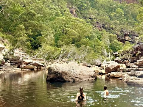 2 people swim in a secluded swimming hole among cliffs and iconic Australian flora