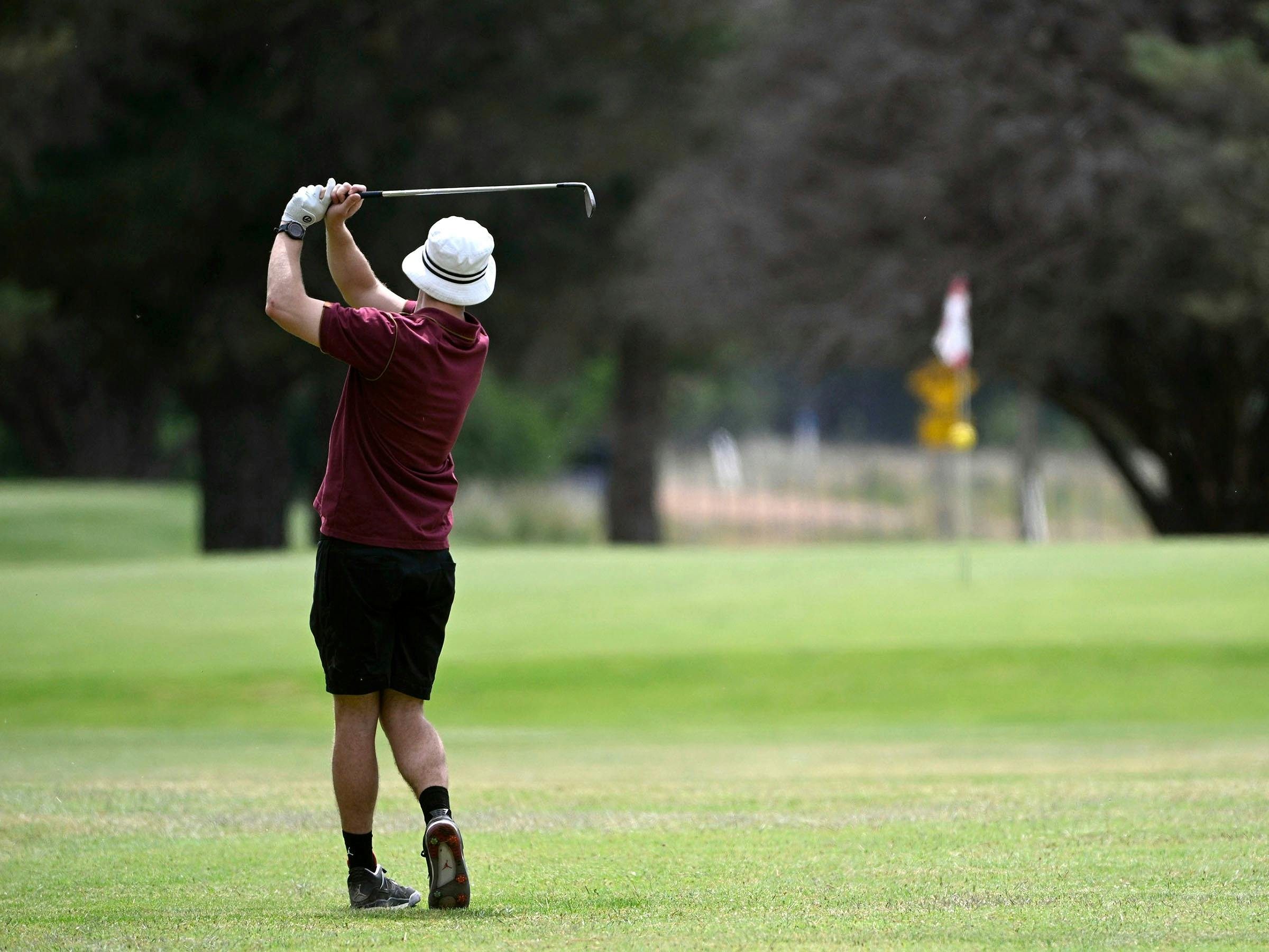 A golfer watches his shot approach the green.