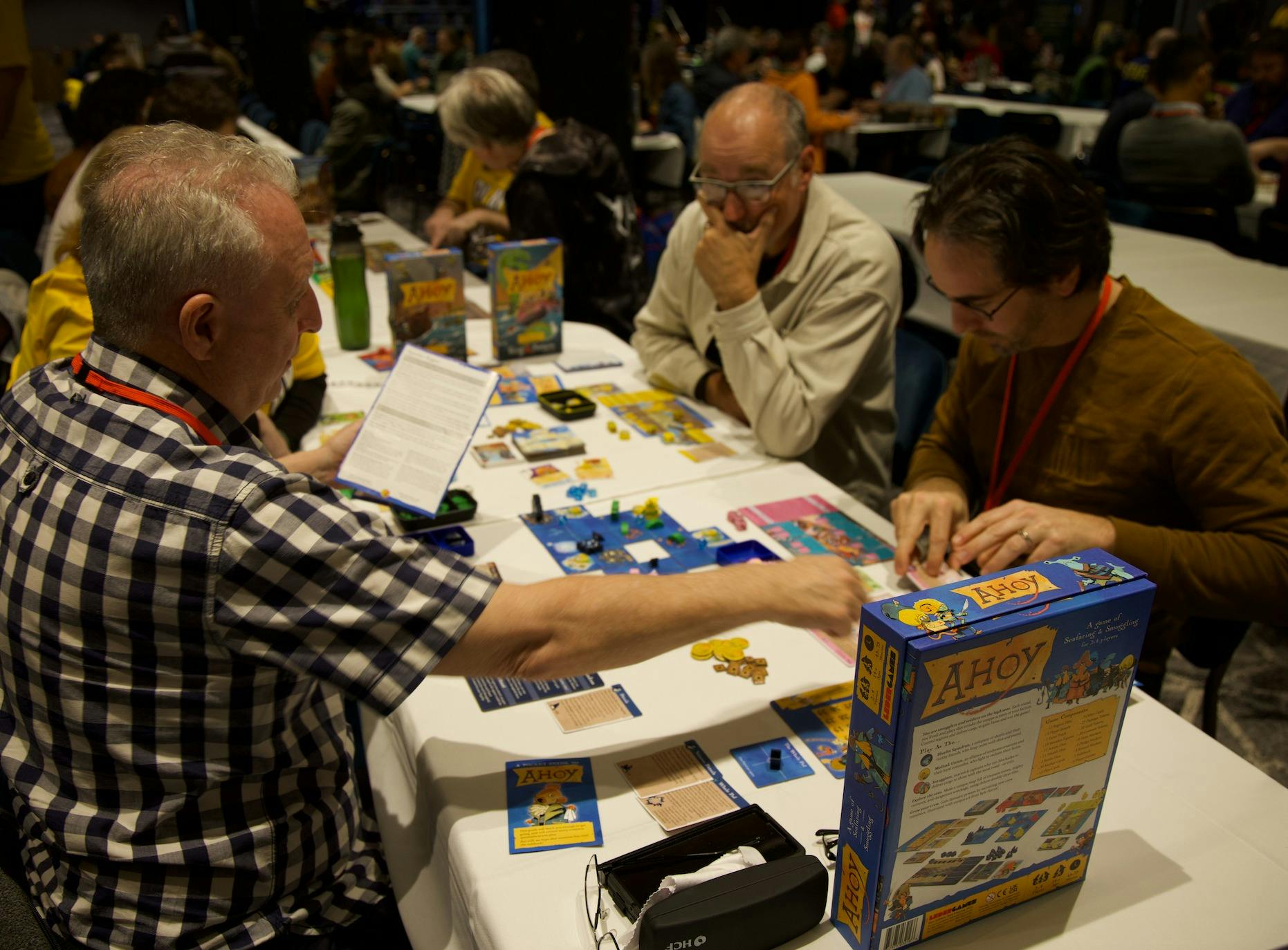 Men sit around the table looking at a board game which one man teaches the game.