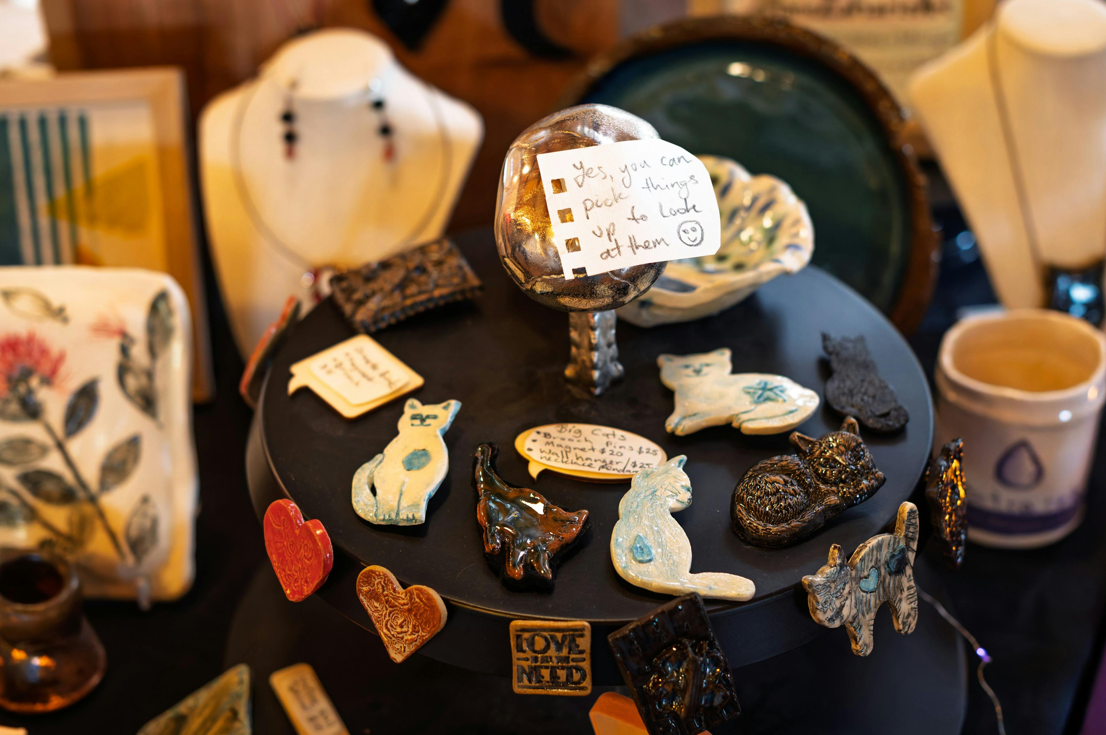 A close-up of handmade brooches on a market table, some shaped like cats.