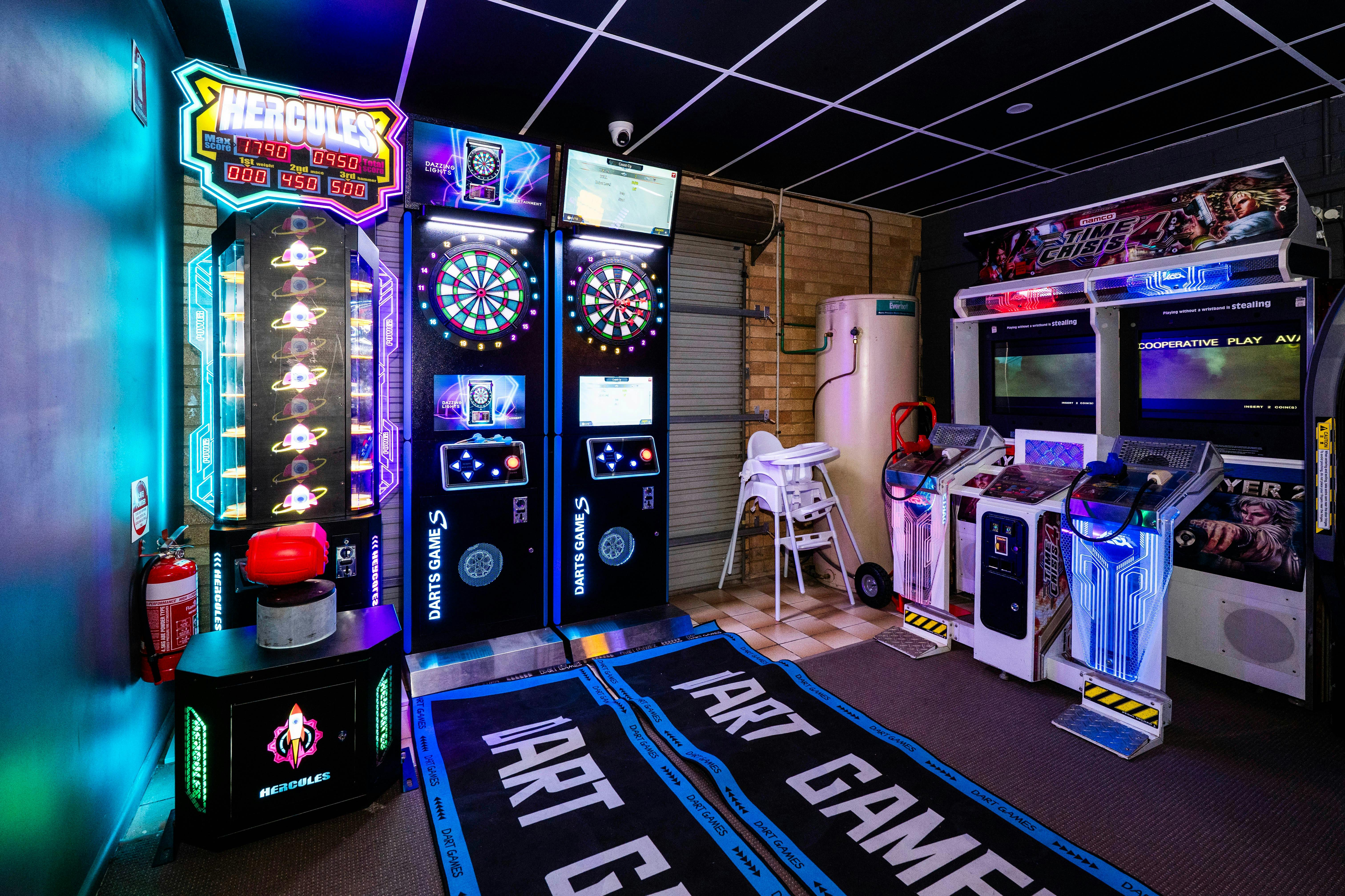 Arcade gaming area with bright LED-lit machines lined up, including hammer machine and darts