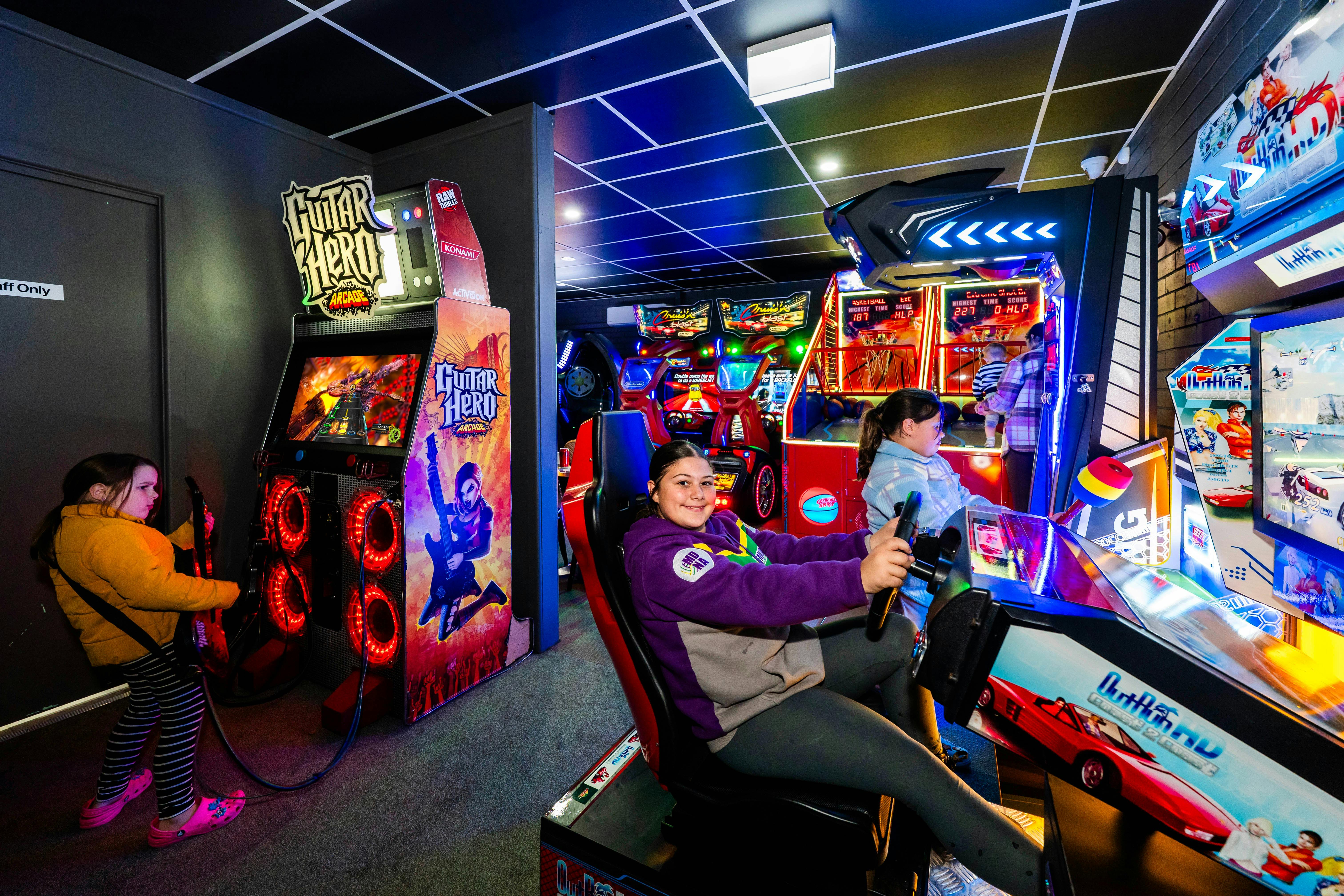 Colorful arcade room with neon lights, including racing games, guitar games and retro machines