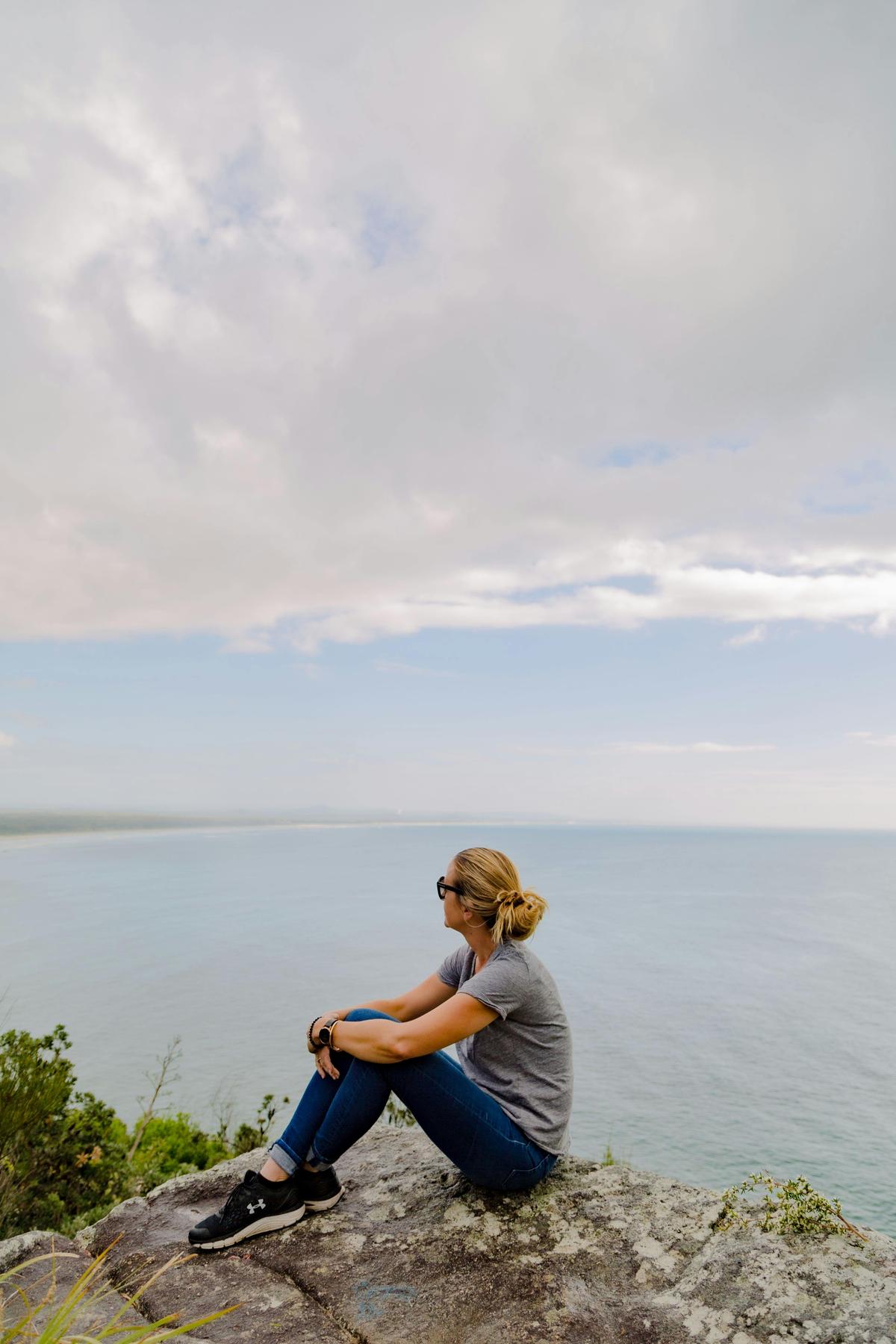 Lady sitting on a rock at a lookout. Ocean is in the background.
