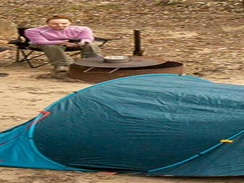 2 campers sitting next to a fire pit barbecue behind their tent. Photo: John Spencer/DPIE