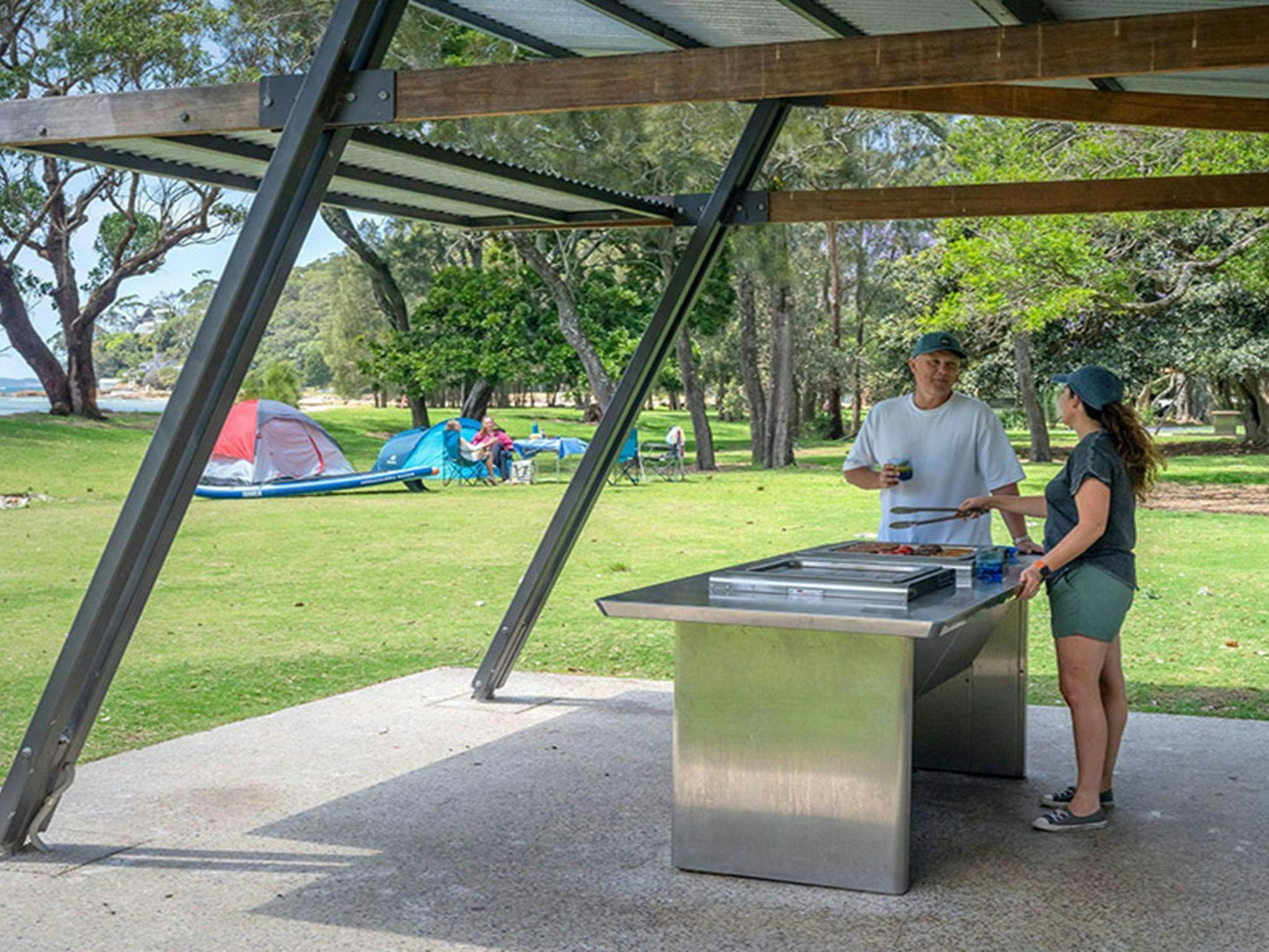 2 people using a sheltered barbecue at Bonnie Vale campground in Royal National Park. Credit: John